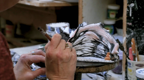 A hand painting pottery, in a screencap from the documentary 'Catching a Glimpse Of Beauty'